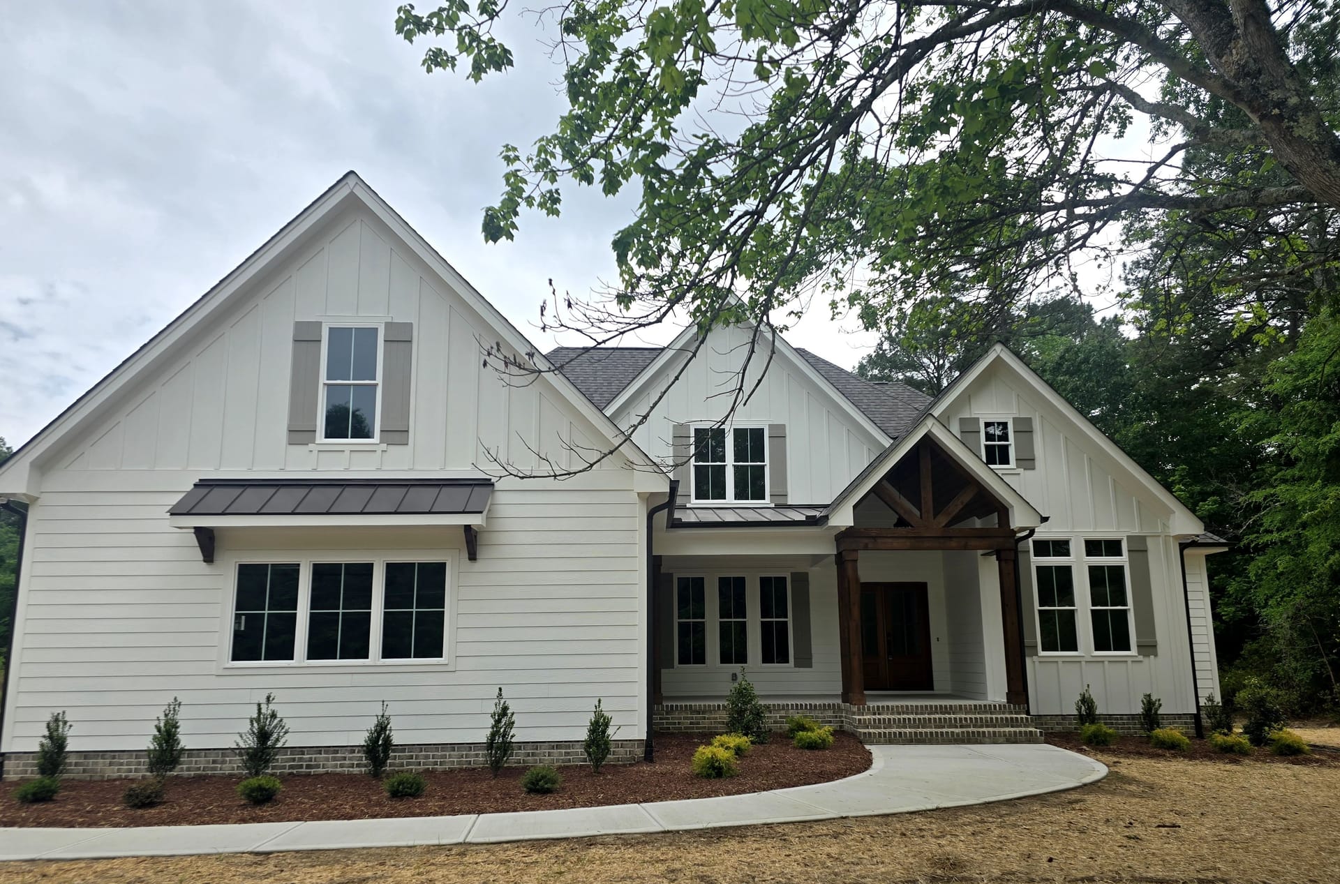 A newly painted white farmhouse-style home with dark trim and a timber-framed porch